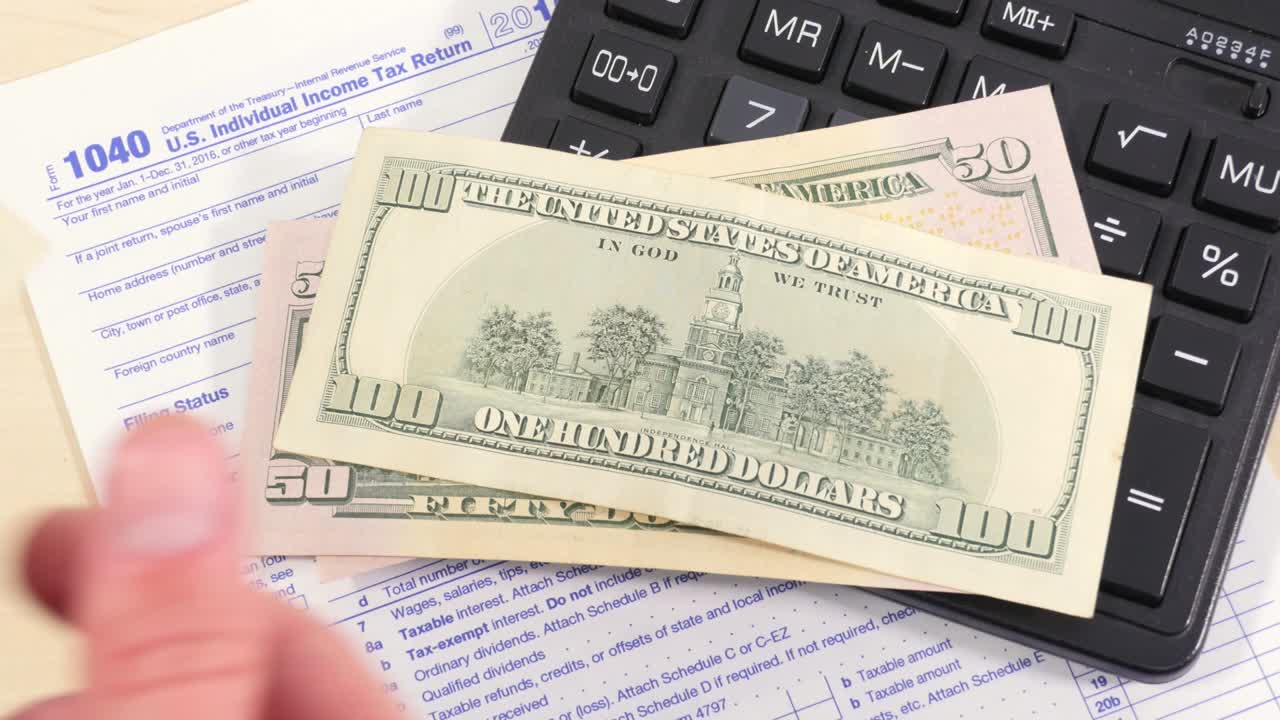 las manos de los hombres lanzan varios billetes de cientos de dólares sobre la mesa con una calculadora y un formulario de impuestos.