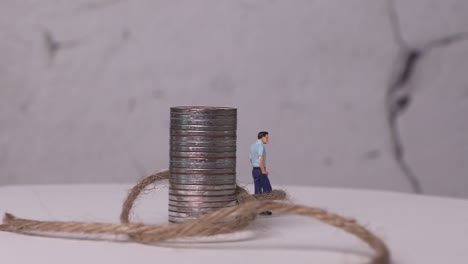 a miniature man woven with piles of coins and ropes.