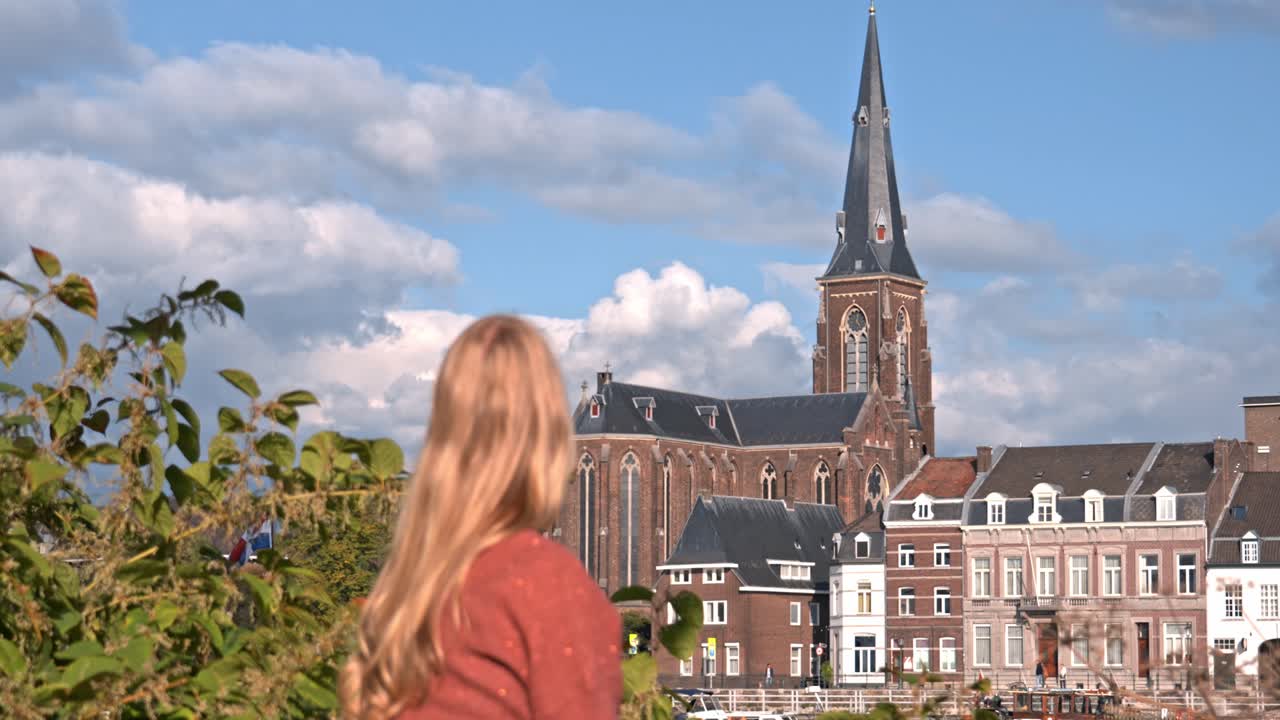Woman standing on the riverbank in Maastricht, Netherlands, with the striking Sint-Martinuskerk (St. Martin's Church) as a prominent feature in the background