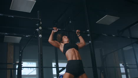 female athlete swinging on chin up bar. strong women doing chin-ups on gymnastic bars in gym. professional athlete does chin-up power strength and cross fitness exercises and everyday workout routine.