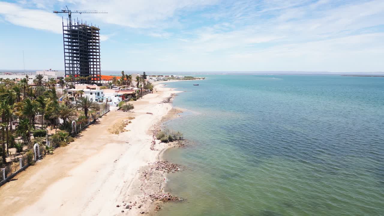 Coastal view with calm sea, tall building under construction, palm trees, La Paz Mexico