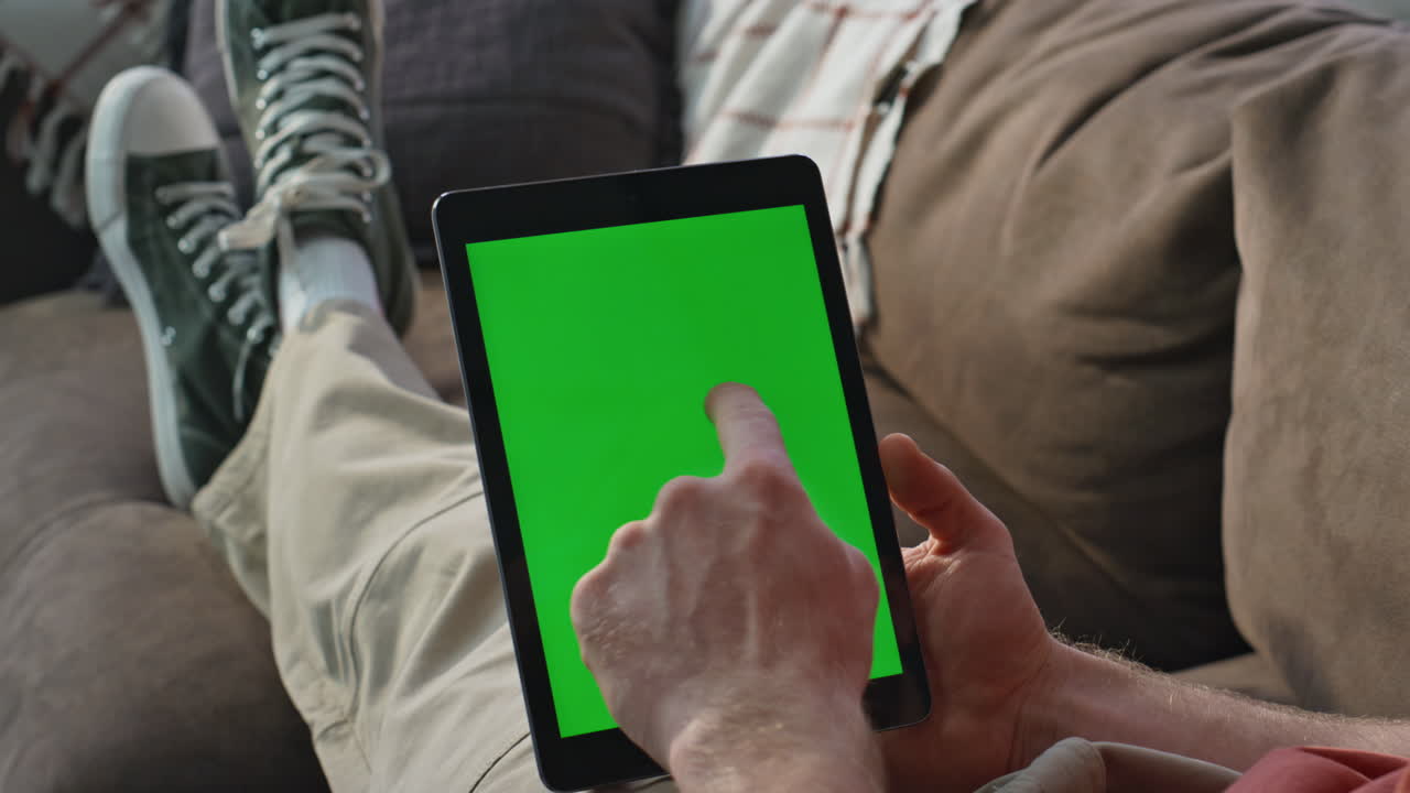 Hand swiping chromakey tablet sitting comfortable at apartment couch closeup