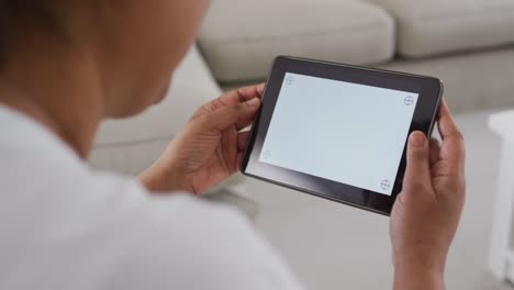 African-american-senior-woman-sitting-on-couch-using-tablet,-with-copy-space-on-screen