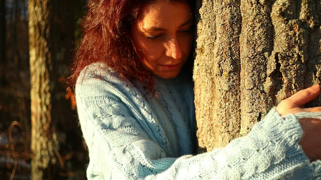 young red hair caucasian girl hugging a tree in the woods at sunset, zoom in close up shot