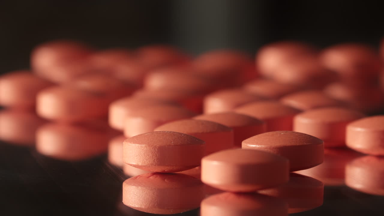 많은 작은 분홍색 빨간색 처방약 알약이 어두운 거울 표면에 쏟아졌습니다.