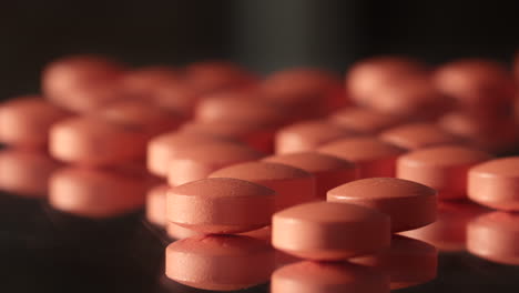 many small pink red prescription drug pills tablets spilled across dark mirrored surface close up