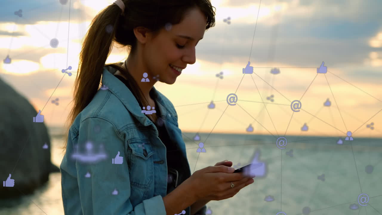 red de iconos digitales contra una mujer caucásica que usa un teléfono inteligente sentada cerca del mar