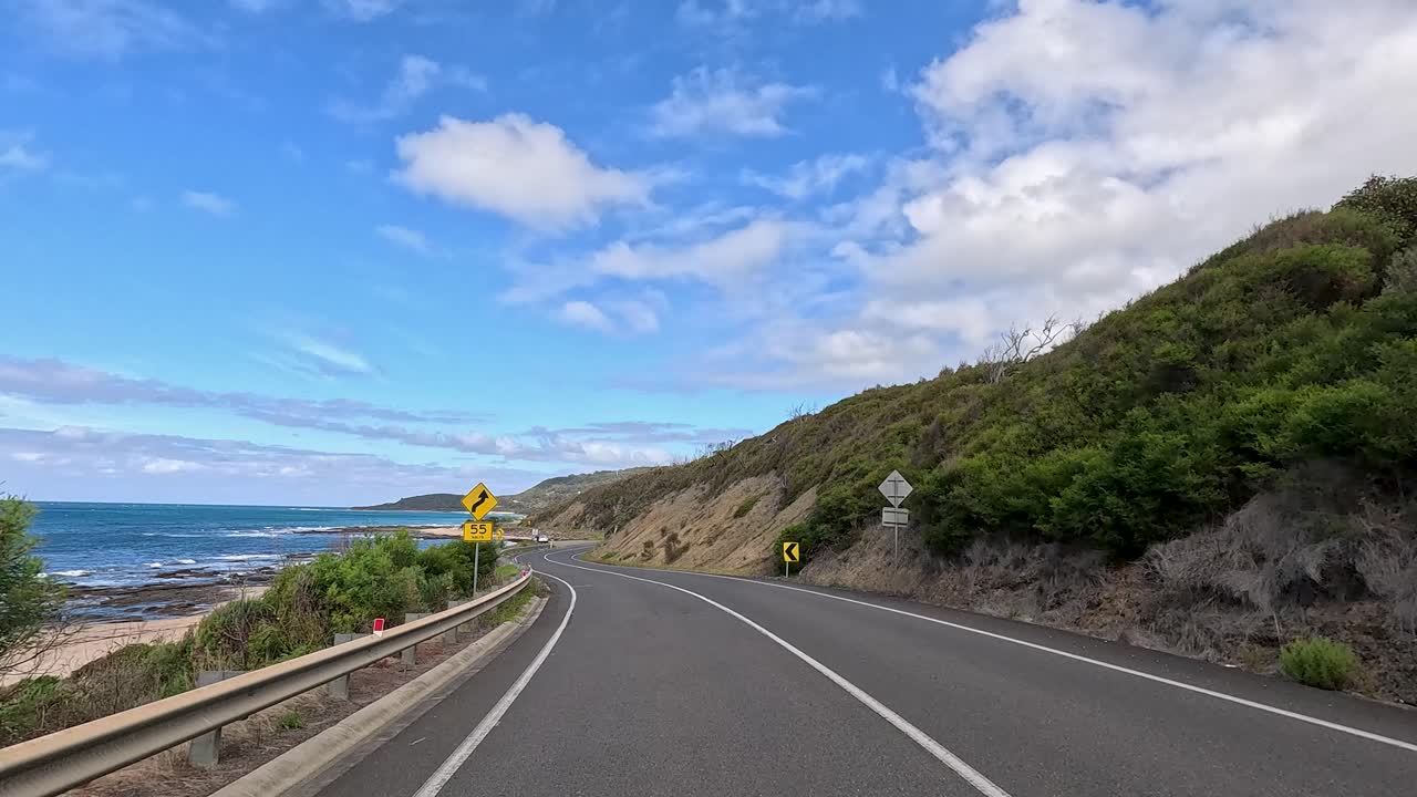 A serene drive on Great Ocean Road, showcasing coastal views, winding roads, and lush greenery under a bright blue sky