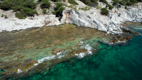 backwards drone movement slowly revealing aliki ancient marble quarry with turquoise water and high mountain peaks in the background, thassos, greece