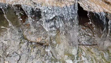 flowing-waterfall-from-a-mountain-spring-water-stream-running-down-huge-sandstone-slabs-of-rock-with-green-moss,-crystal-clear-drinking-water,-meditate-tranquil-and-peaceful-calm-slow-motion-footage