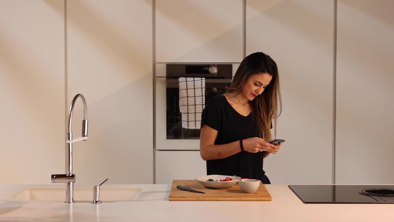 Donna che chatta sullo smartphone in cucina.