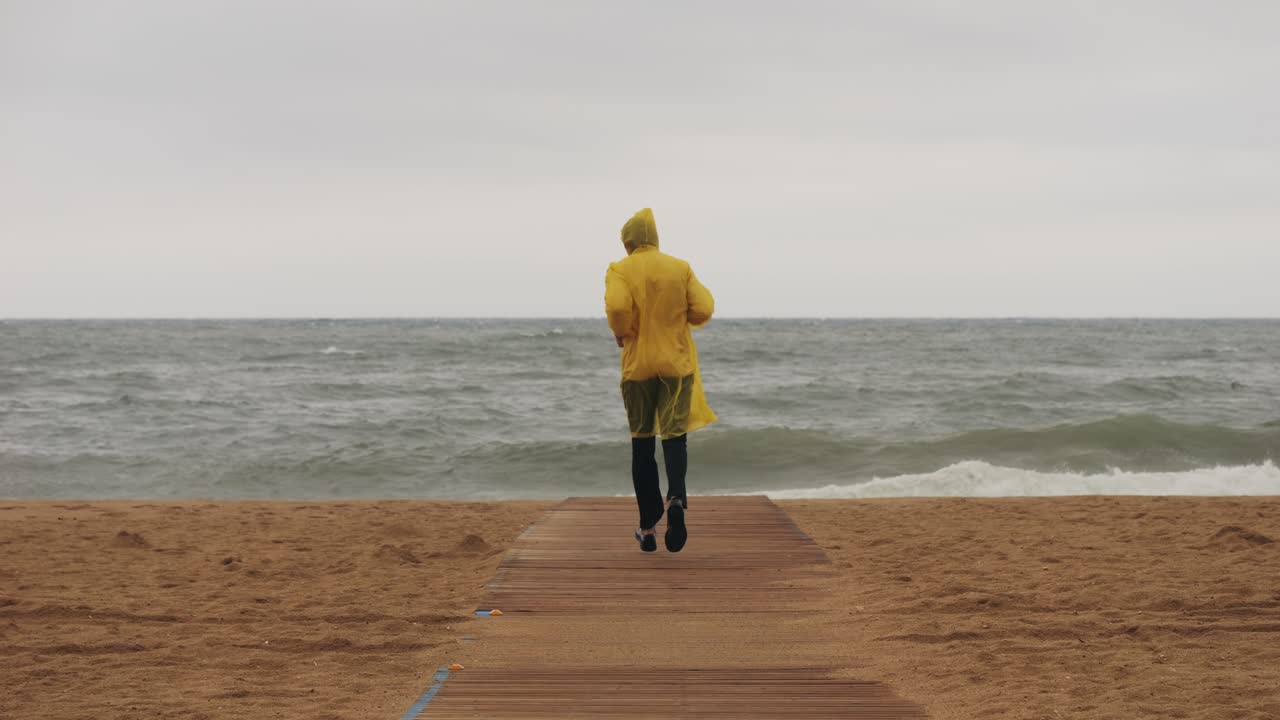 Man tourist person with umbrella and raincoat near sea ocean beach with storm on rainy european city street, lights reflecting, walking in Barcelona or Amsterdam during the rain