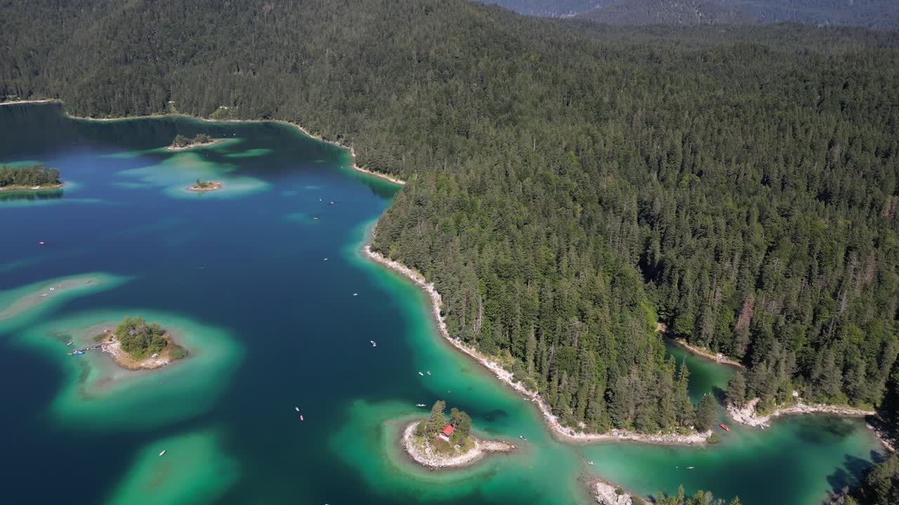 flying over Eibsee bayern Deutschland shallow depth lake blue turquoise colorful water in the middle of pine tree forest in a summer morning time hazy day Europe mountain in wonderful scenic landscape