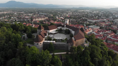 drone disparado volando sobre el castillo de ljubljana con la ciudad detrás y inclinándose hacia el patio del castillo