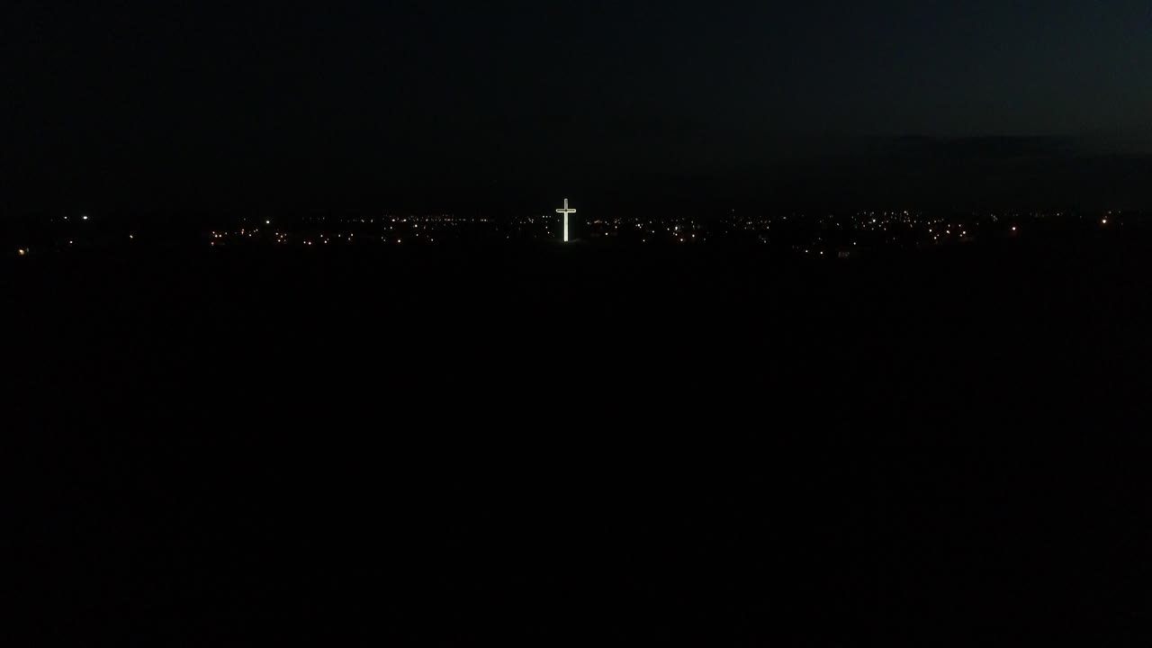 밤에 도시의 불빛을 배경으로 언덕 꼭대기에 불이 켜진 종교 십자가의 와이드 샷