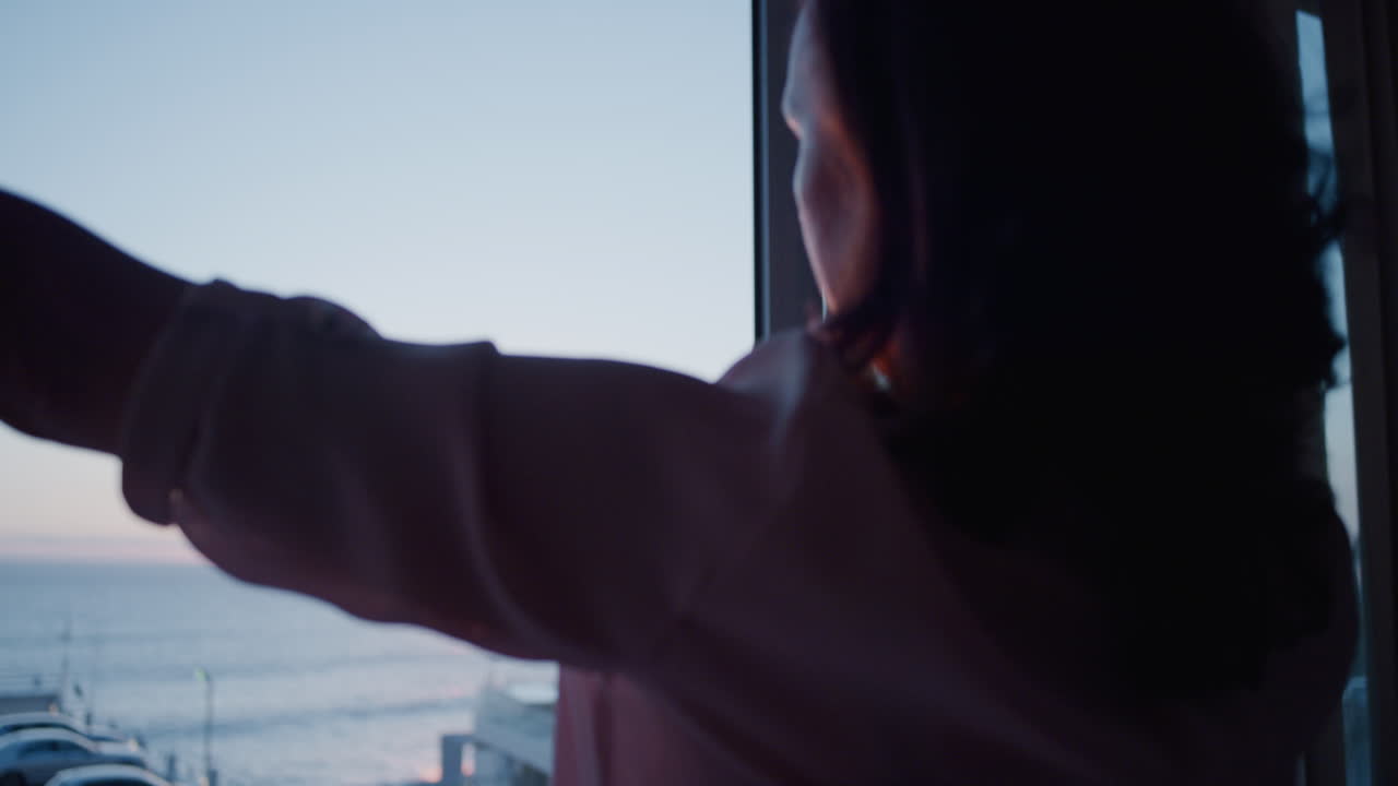 행복한  ⁇ 은 여자가 커튼을 열고 아침 일출을 즐기고 집에서 평화로운 자유를 느끼고 은퇴 휴가에서 휴식을 취하고 아름다운 바다 전경을 바라보고 있습니다.