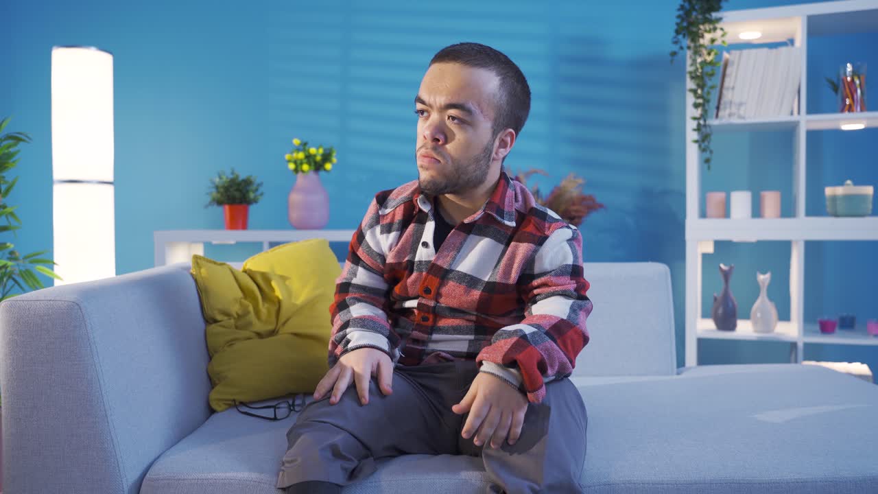 joven con enanismo discapacitado sentado en el sofá en casa se enoja y es agresivo.