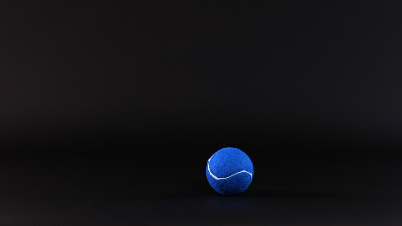 A blue tennis ball rolls across a surface