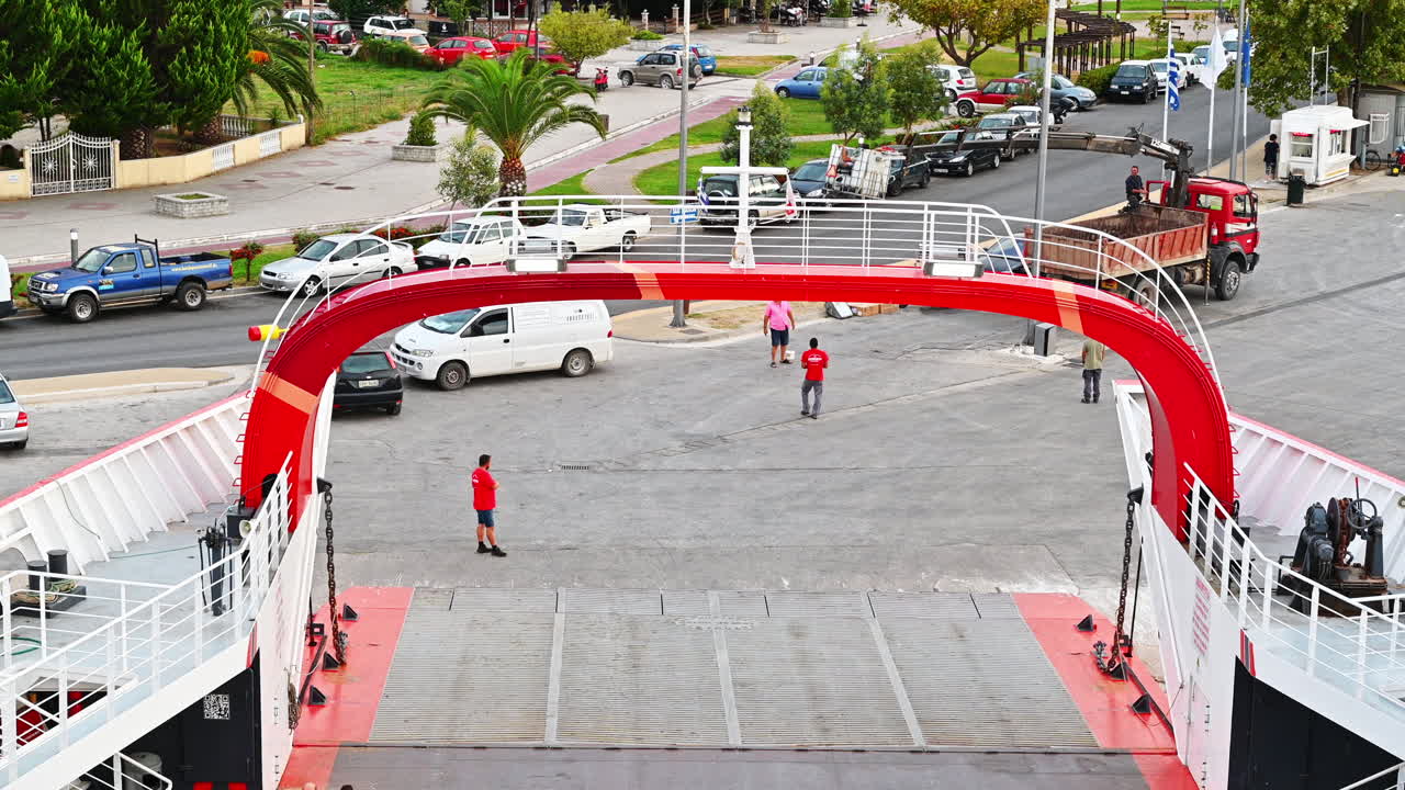THASOS, GREECE - SEPTEMBER 23, 2020: Moored ferryboat, opened gangplank in the port, road, walking people, town and parked cars on the background
