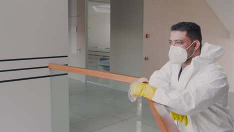 hombre árabe con equipo de protección personal mirando la cámara mientras se quita la máscara dentro de un edificio de oficinas