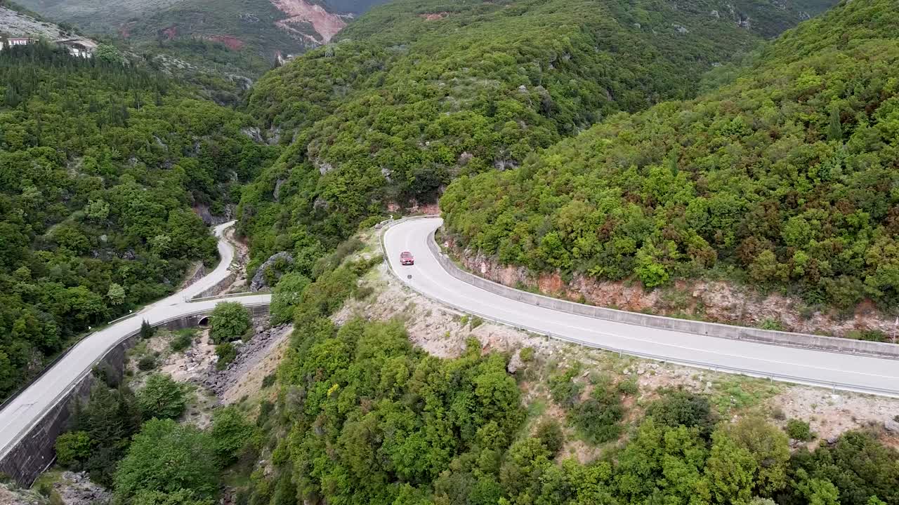알바니아의 푸른 산맥의 휘어지는 도로를 가로질러 운전하는 자동차의 공중 촬영