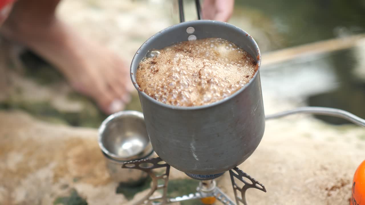 Kokande vatten och snabbkaffe på campingkök nära flod