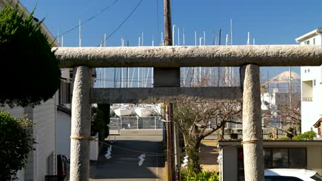 Japanese-stone-Torii-gate-with-backdrop-of-fishing-boats-and-Mt