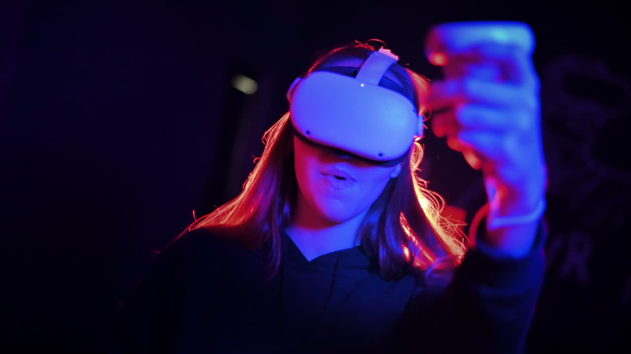 A young interested woman playing in VR games using VR glasses and controllers. Red and blue illumination. Slow motion