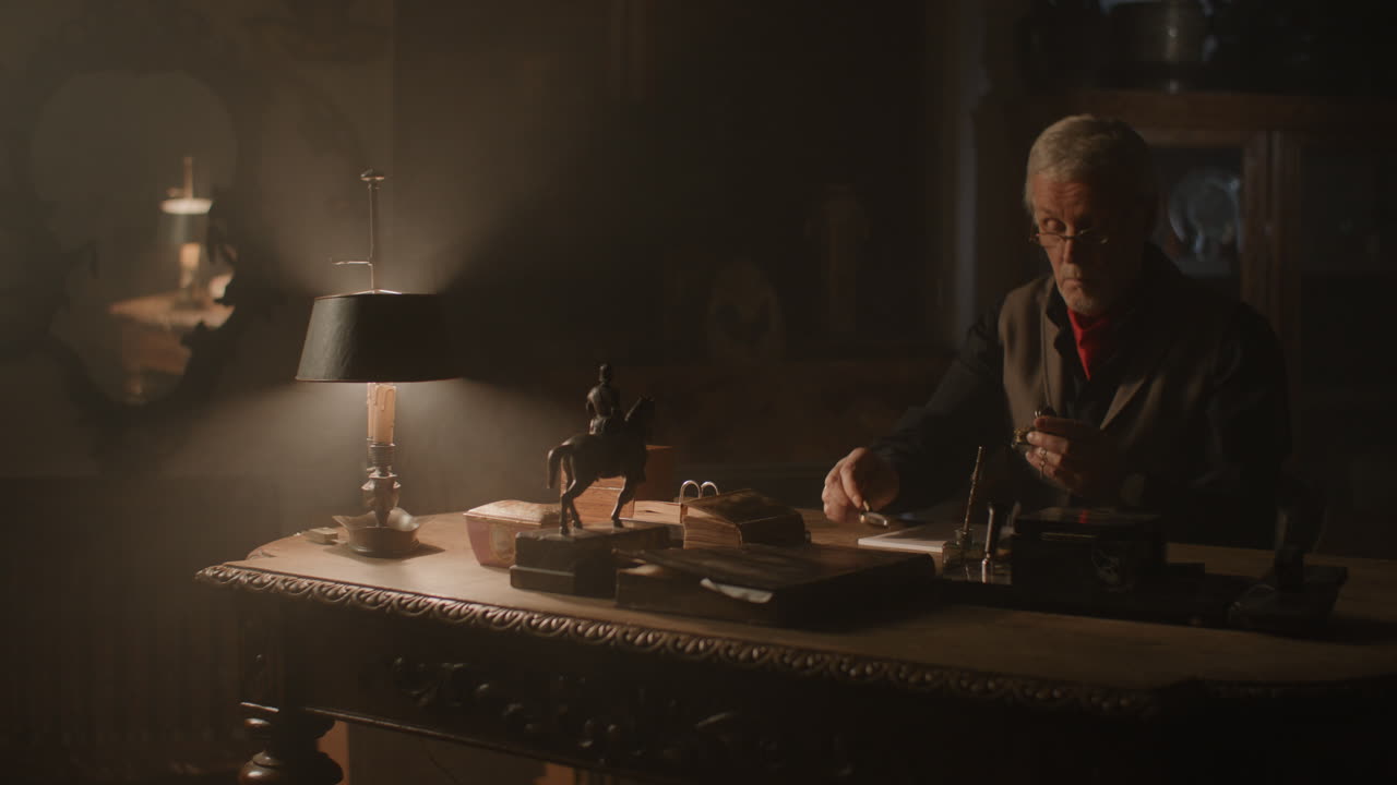 Older passionate man evaluates an old silver skull watch in his office at night