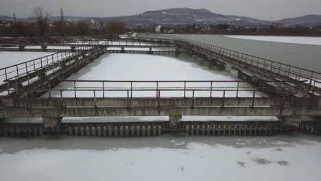 Frozen-lake-in-winter,-aerial-drone-shot-from-above,-concrete-walkways-in-lake,-dark,-cloudy-and-moody-scene,-forward-dolly-shot