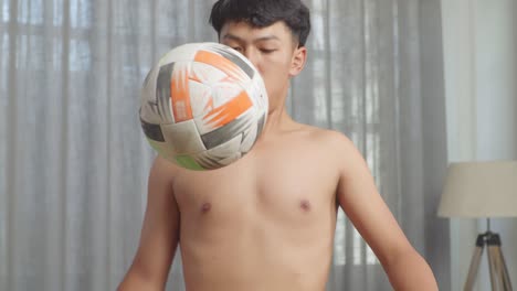 primer plano de un adolescente asiático haciendo habilidades de fútbol durante el entrenamiento sin camisa en casa