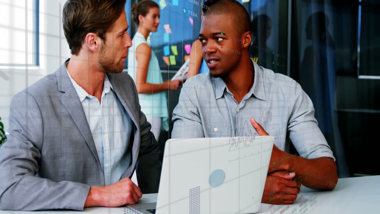 Animation of stock market data processing over two diverse men discussing over a laptop at office