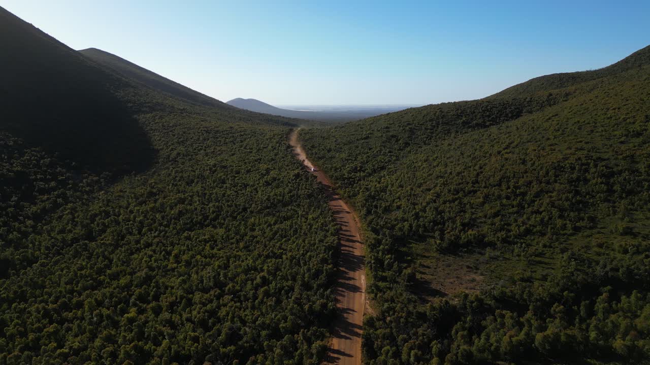 toma aérea de cuatro ruedas motrices en camino de tierra roja en el interior australiano, montañas a ambos lados