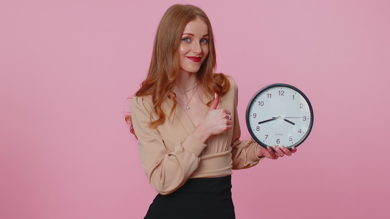 Businesswoman girl showing time on office clock ok thumb up approve pointing finger at camera