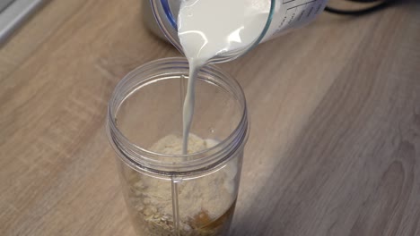 milk being poured into a blender containing oats and other ingredients, ready for blending