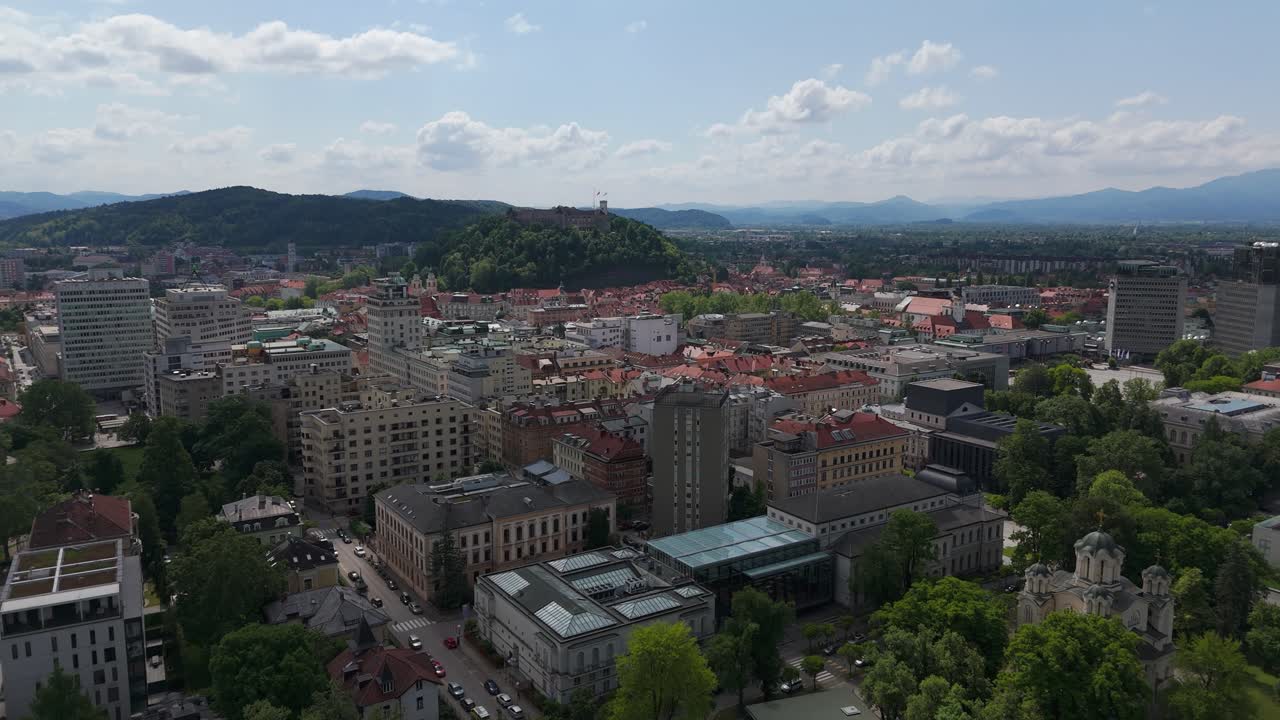 Aerial: view of Ljubljana city center with castle rising above the capital city of Slovenia during the day, establishing drone shot