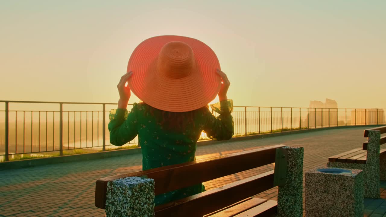 A serene moment at sunset, featuring a woman in a pink hat sitting on a bench, enjoying the golden glow and peaceful ambiance of the evening sky and landscape