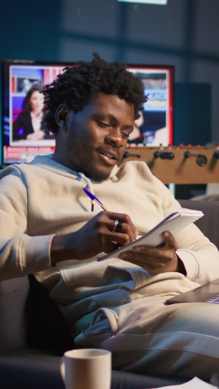 Young African American Man Writing Notes on Couch at Home