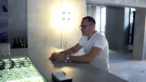 an-adult-man-in-glasses-sits-at-the-bar-counter-and-takes-a-sip-of-a-red-colored-cocktail