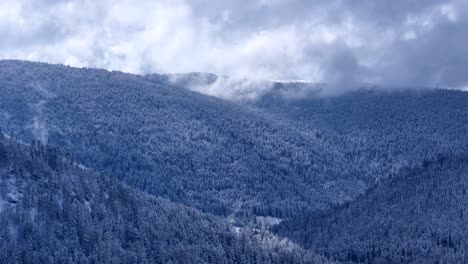 Drones-En-órbita-Lenta-Vuelan-Sobre-El-Paisaje-Montañoso-Cubierto-De-Nieve-Durante-La-Primavera-Con-Cielo-Azul-Y-Grandes-Nubes