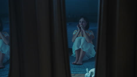 a traumatised and disoriented girl sits on the bedroom floor