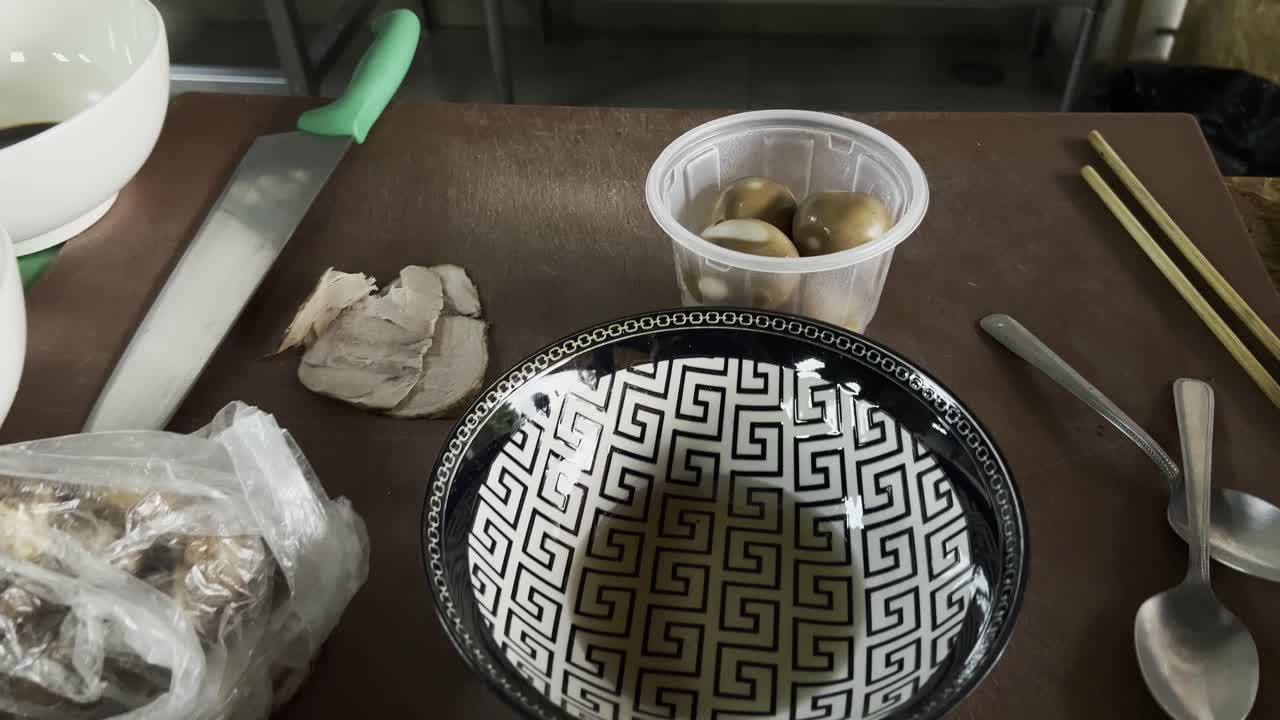 Overhead close-up of marinated ramen eggs and pork slices on kitchen counter with bowl and knife