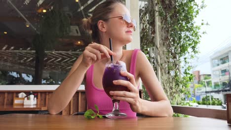 mujer disfrutando de una bebida púrpura en un café al aire libre