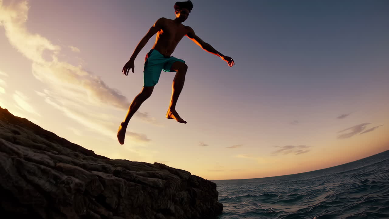 Man jumping from a cliff into the ocean at sunset