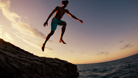 man jumping from a cliff into the ocean at sunset