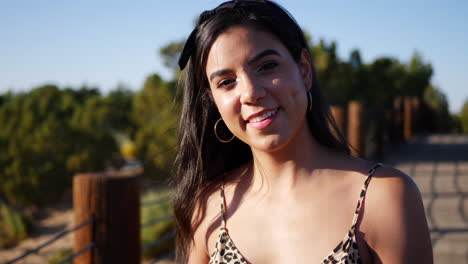 An-attractive-young-hispanic-woman-traveler-walking-and-smiling-on-a-nature-path-in-slow-motion-in-sunset-light