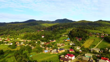 vista aérea sobre casas, bosque y naturaleza verde iluminada por el sol, en el pueblo de myhove, de las montañas de los cárpatos, hora dorada, en ucrania - pan, disparo de drone