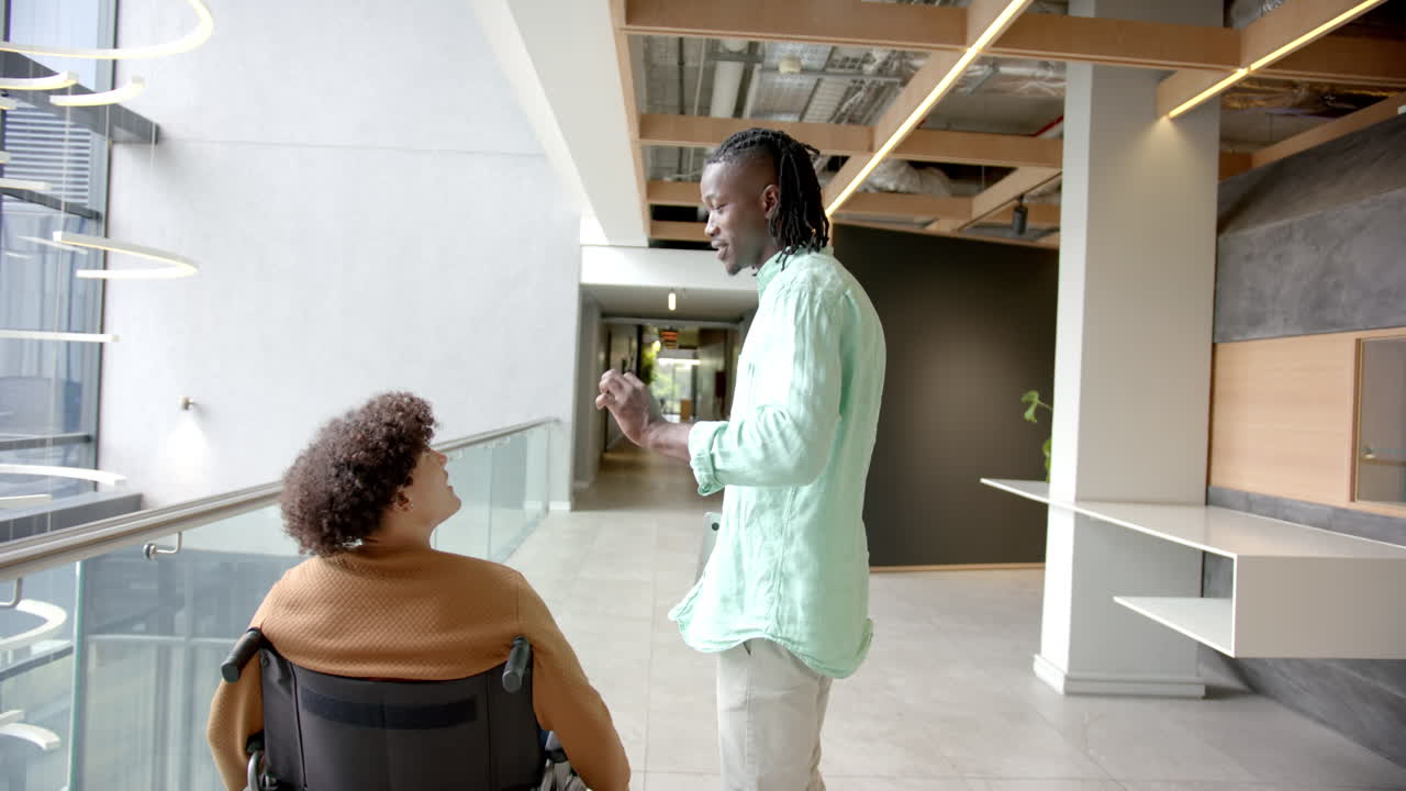 Walking in hallway, man talking to colleague in wheelchair at modern office