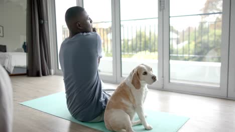 african american man doing yoga and stretching at home, with his pet dog, slow motion