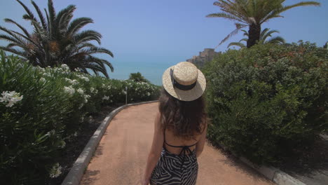 mujer en un sombrero de paja disfrutando de unas vacaciones de verano en la playa con un castillo en el fondo